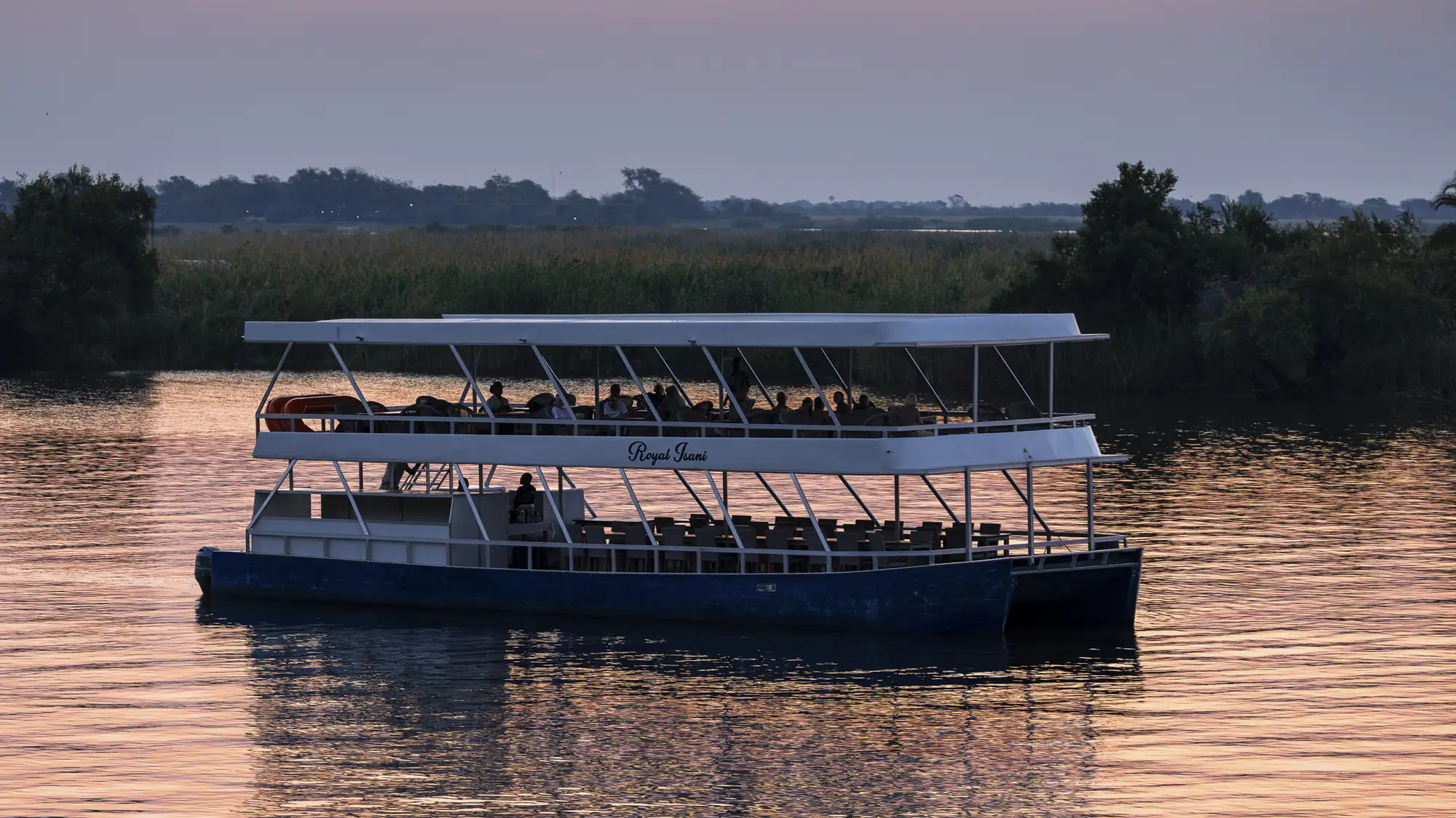 A cruise boat on the Chobe River under a pink dusk sky